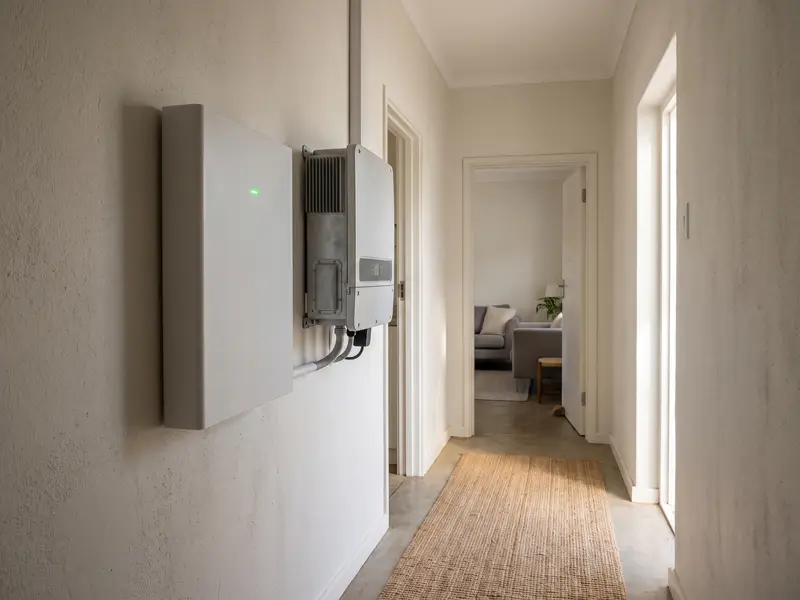 A wall-mounted lithium solar battery next to a hybrid inverter in a house corridor