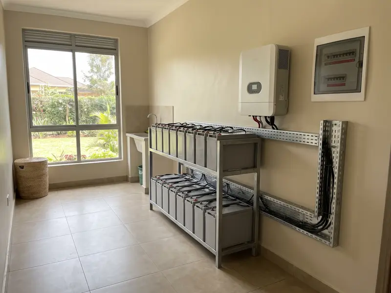 A rack of solar batteries with an inverter and breaker panel in a modern utility room