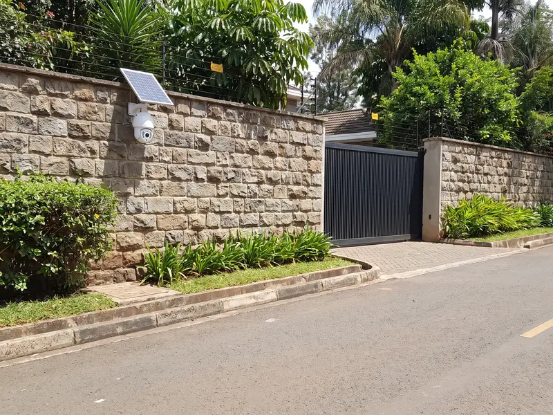A solar-powered CCTV camera on the perimeter wall beside the gate of a modern home