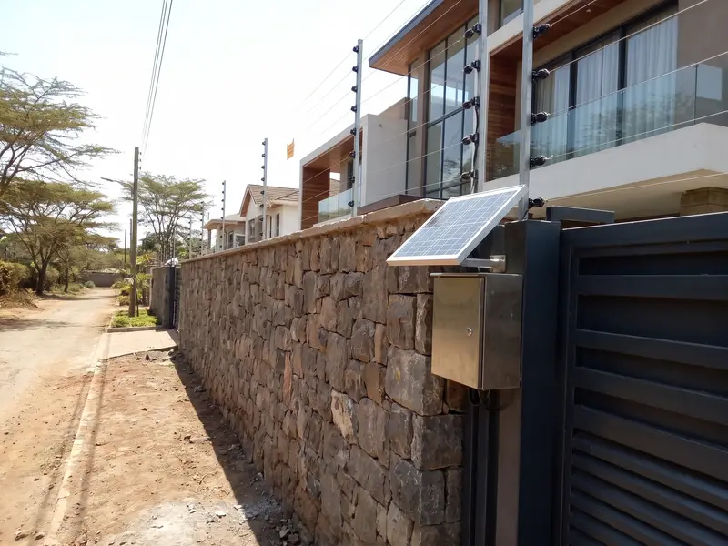 A solar electric fence on the perimeter wall of a modern home, with its panel by the gate